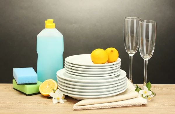 Leere Teller und Gläser mit Spülmittel, Schwämmen und Zitrone auf Holztisch vor grauem Hintergrund — Stockfoto