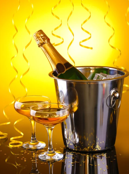 Champagne bottle in bucket with ice and glasses of champagne, on yellow background — Stock Photo, Image