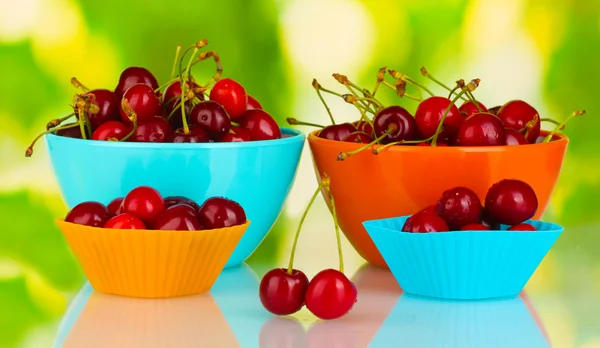 Bowls and cutters with cherries on green background — Stock Photo, Image
