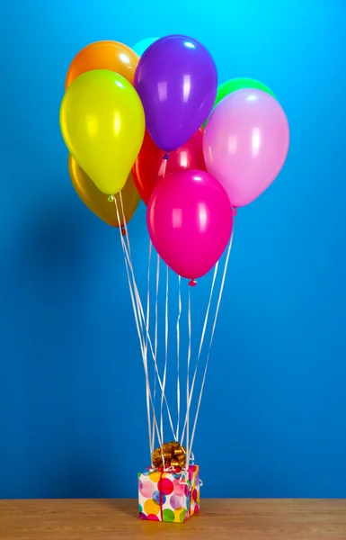 Bunte Luftballons mit einem Geschenk auf einem Holztisch vor blauem Hintergrund — Stockfoto