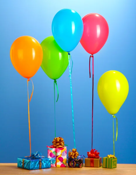 Colorful balloons holding a gifts on a wooden table on blue background — Stock Photo, Image