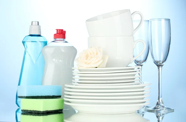 Üres tiszta tányérok, poharak és csészék és folyékony mosogatószer szivacs, kék alapon — Stock Fotó