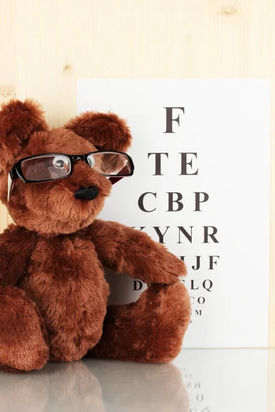Teddy bear with glasses on eyesight test chart background close-up — Stock Photo, Image