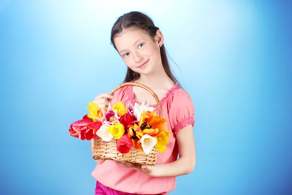 Portrait of beautiful little girl with tulips in basket on blue background — Stock Photo, Image