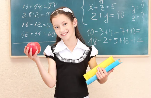 Menina bonita em uniforme escolar com livros e maçã na sala de aula — Fotografia de Stock