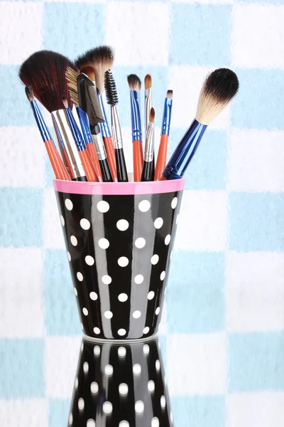 Make-up štětce v černém puntíková cup na barevné pozadí — Stock fotografie