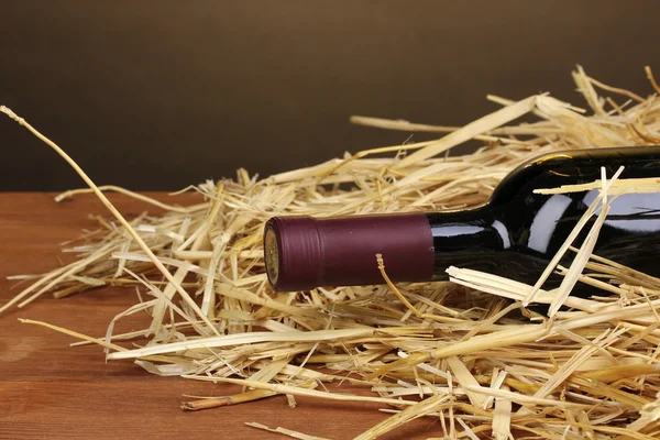 Bouteille de grand vin sur foin sur table en bois sur fond brun — Photo