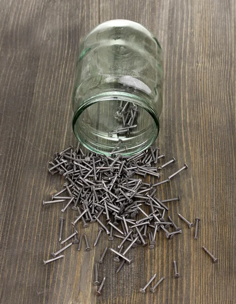 Metalen nagels en glazen pot op houten achtergrond — Stockfoto
