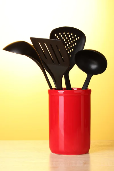 Utensílios de cozinha preto em copo vermelho no fundo amarelo — Fotografia de Stock