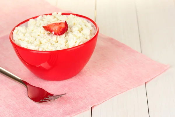 Cottage cheese with strawberry in red bowl and fork on pink napkin on white wooden table close-up — Stock Photo, Image