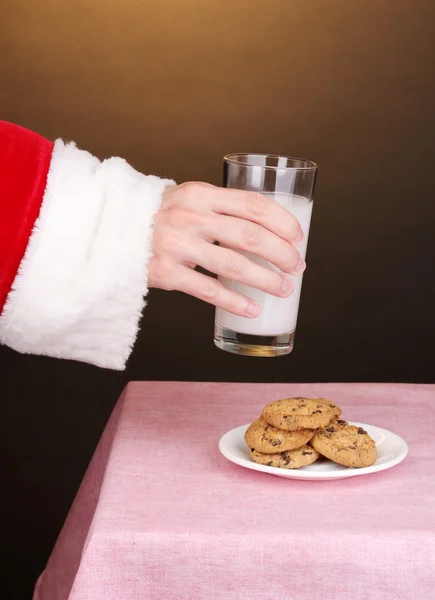 Рука Санта-Клауса держит стакан молока на коричневом фоне — стоковое фото