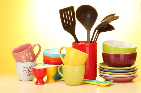 Cuencos vacíos brillantes, tazas y utensilios de cocina sobre mesa de madera sobre fondo amarillo —  Fotos de Stock