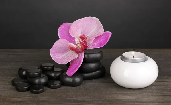 Spa kamienie z orchidea kwiat i świeca na drewnianym stole na szarym tle — Zdjęcie stockowe