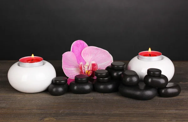 Wellness-Steine mit Orchideenblume und Kerzen auf Holztisch auf grauem Hintergrund — Stockfoto