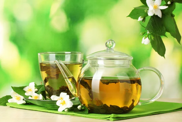Zelený čaj s Jasmín v poháru a konvici na dřevěný stůl na zeleném pozadí — Stock fotografie
