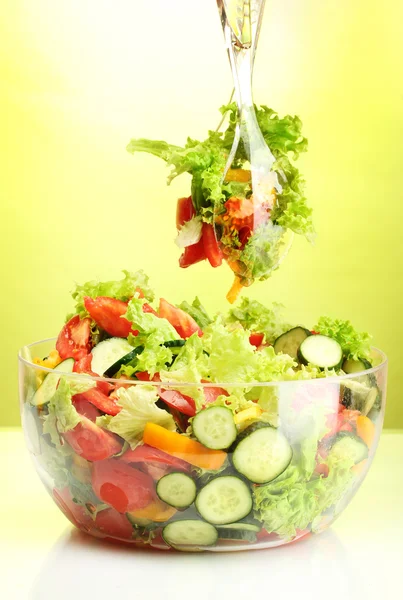 stock image Fresh vegetable salad in transparent bowl with spoon and fork on green background