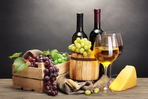 Barrel, bottles and glasses of wine, cheese and ripe grapes on wooden table on grey background — Stock Photo, Image