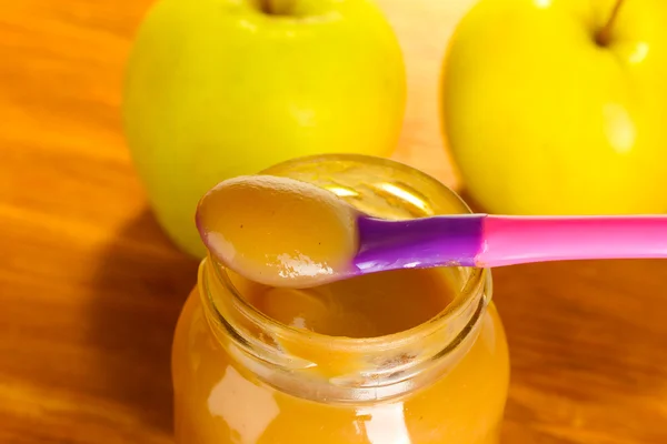 Glas mit Apfel-Babynahrung, Löffel und Äpfeln auf Holztisch in Großaufnahme — Stockfoto