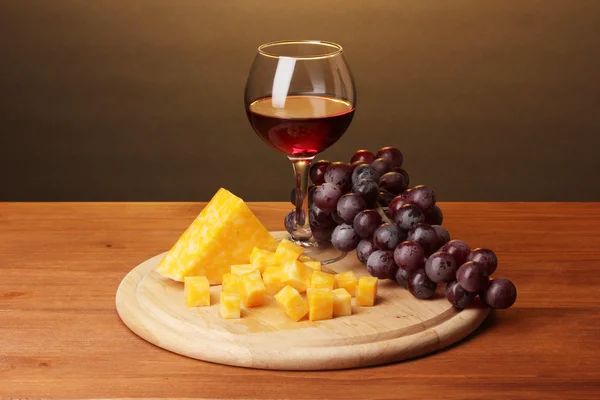 Wine in wineglass and cheese on wooden table on brown background — Stock Photo, Image