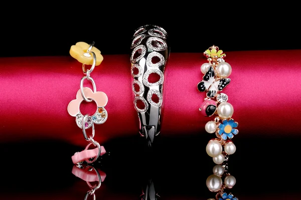 Três belas pulseiras no pano rosa no fundo preto — Fotografia de Stock