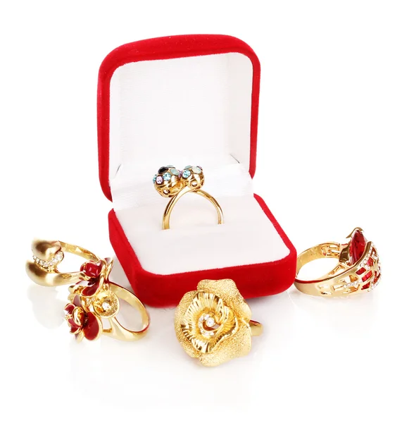 Anel de ouro com cristais azuis, pretos, lilás e claros em caixa de veludo vermelho e quatro anéis dourados isolados em branco — Fotografia de Stock