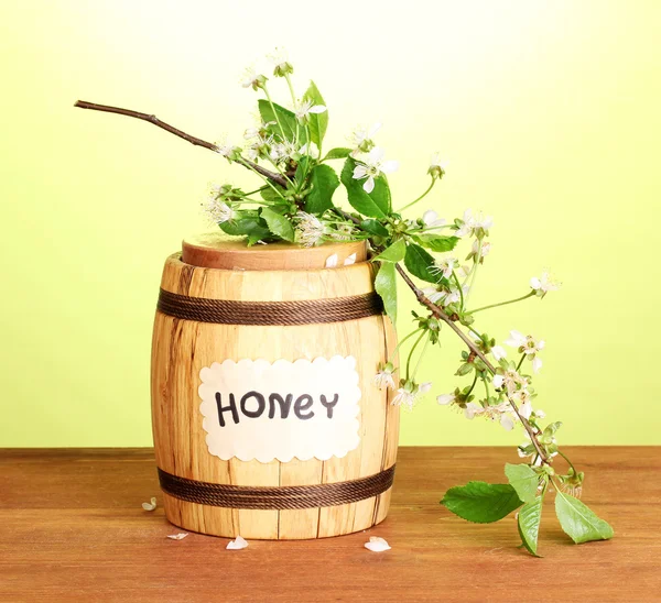 Сладкий мед в бочке с цветущей веткой на деревянном столе на зеленом фоне — стоковое фото