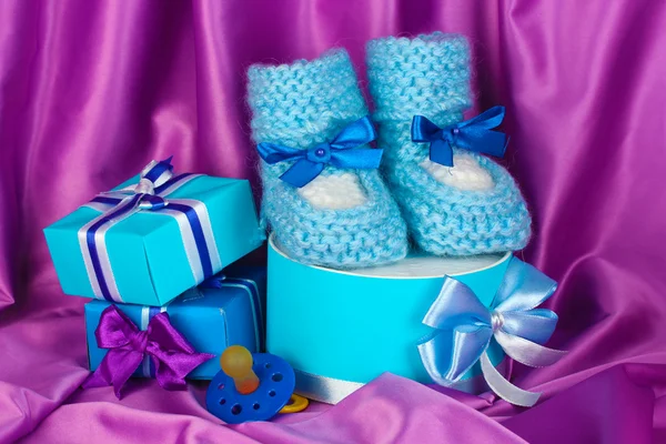 Blue baby boots, pacifier, gifts on silk background — Stock Photo, Image