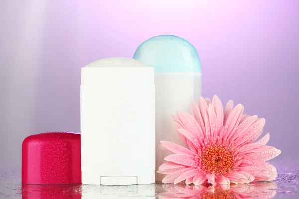 Deodorant botttles met bloem op paarse achtergrond — Stockfoto