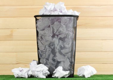 Metal trash bin from paper on grass on wooden background clipart