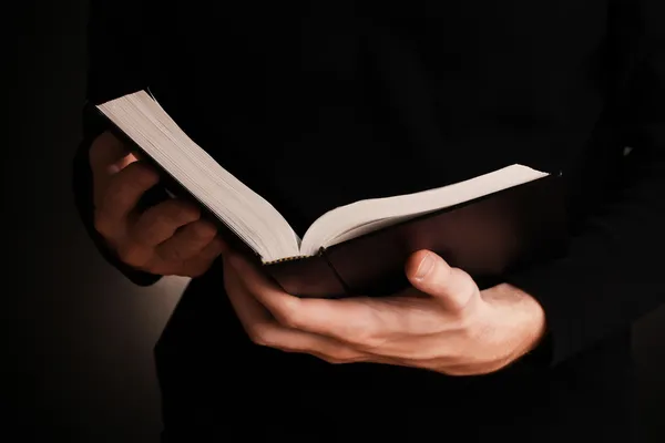 Hände mit offener russischer Bibel auf schwarzem Hintergrund — Stockfoto