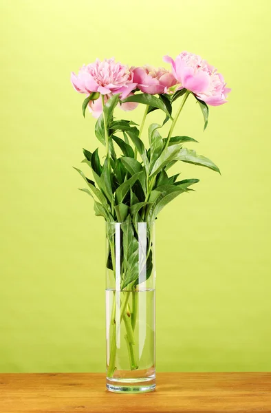 Three pink peonies in vase on wooden table on green background — Stock Photo, Image