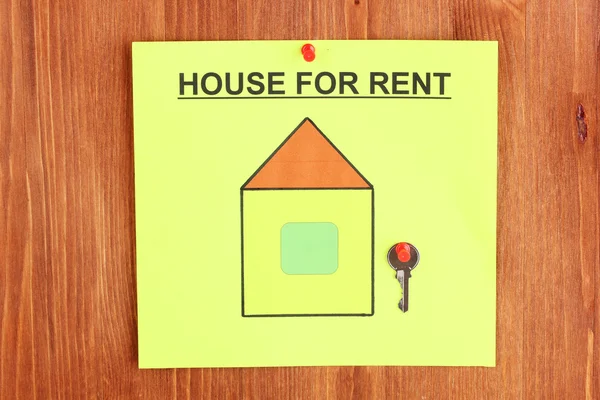 Cartaz sobre alugar a casa com a chave no fundo de madeira close-up — Fotografia de Stock
