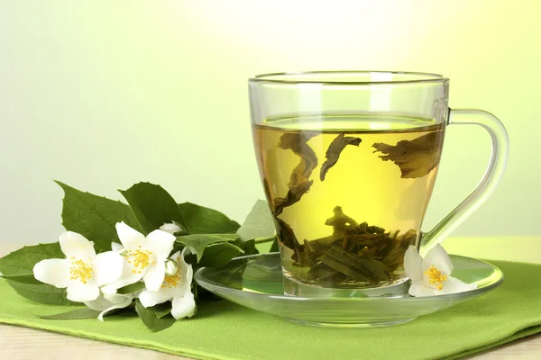 Kopp grönt te med Jasmin blommor på träbord på grön bakgrund — Stockfoto