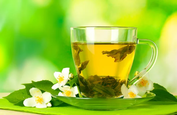 Tasse de thé vert avec des fleurs de jasmin sur table en bois sur fond vert — Photo