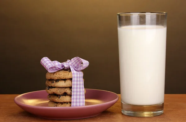 Glas Milch und Kekse auf Holztisch auf braunem Hintergrund — Stockfoto