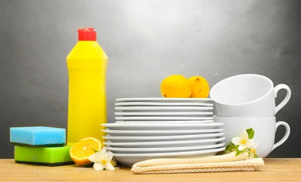 Prázdné čisté talíře, sklenice a kelímky s mytí nádobí, houby a citron na dřevěný stůl na šedém pozadí — Stock fotografie