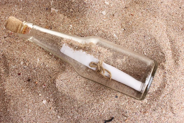 Скляна пляшка з нотою на піщаному березі з черепашками — стокове фото
