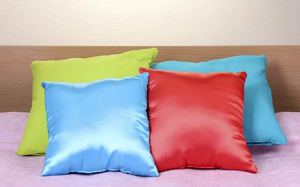 Cuscini luminosi sul letto su sfondo beige — Foto Stock