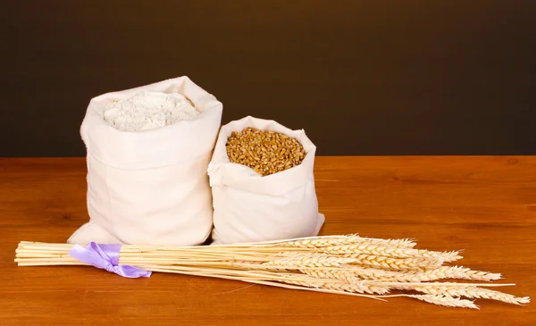 Meel en tarwe graan op houten tafel op donkere achtergrond — Stockfoto
