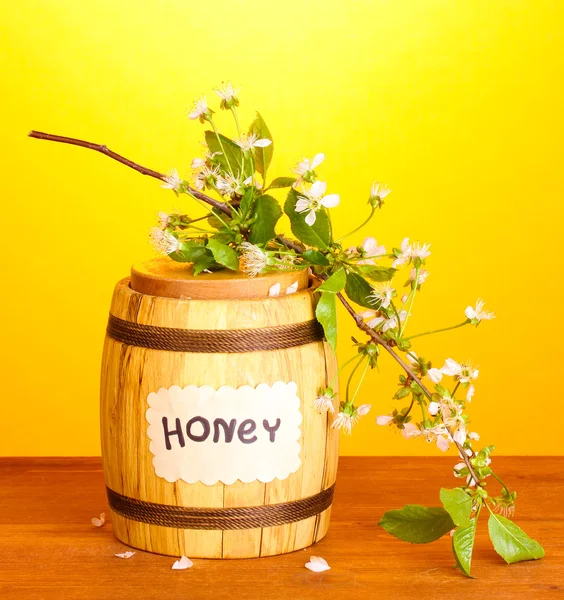 Miel dulce en barrica con rama floreciente sobre mesa de madera sobre fondo amarillo —  Fotos de Stock