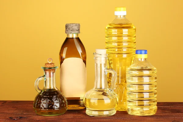 Оливковое и подсолнечное масло в бутылках и маленьких графинах на жёлтом фоне крупным планом — стоковое фото