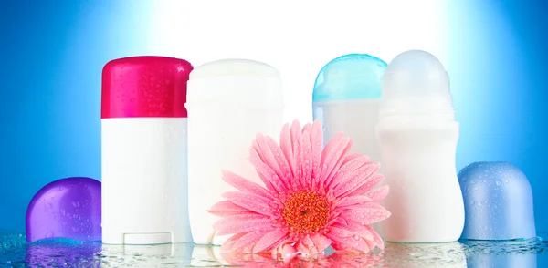 Botellas de desodorante con flor sobre fondo azul — Foto de Stock
