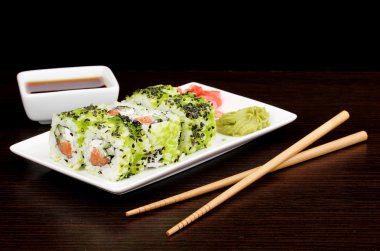 Tasty rolls served on white plate with chopsticks on wooden table on black background clipart