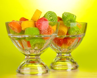 Colorful jelly candies in in glass bowls on green background clipart