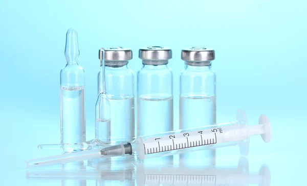 Jeringa y ampollas médicas sobre fondo azul — Foto de Stock