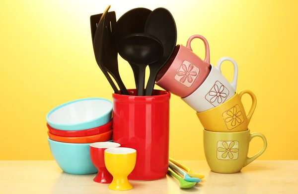 Яркие пустые миски, чашки и кухонные принадлежности на деревянном столе на желтом фоне — стоковое фото