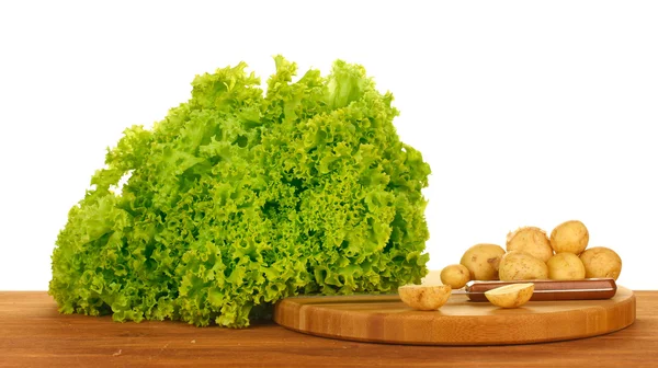 Young potatoes and lettuce on a cutting board with knife on a table on white background close-up — Stock Photo, Image