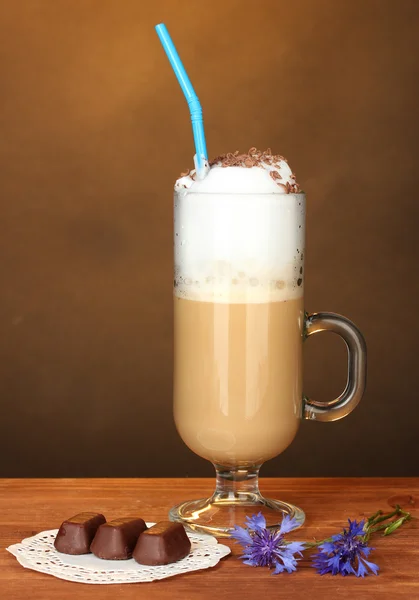 Glas Kaffee-Cocktail mit Schokoladenbonbons auf Deckchen auf braunem Hintergrund — Stockfoto
