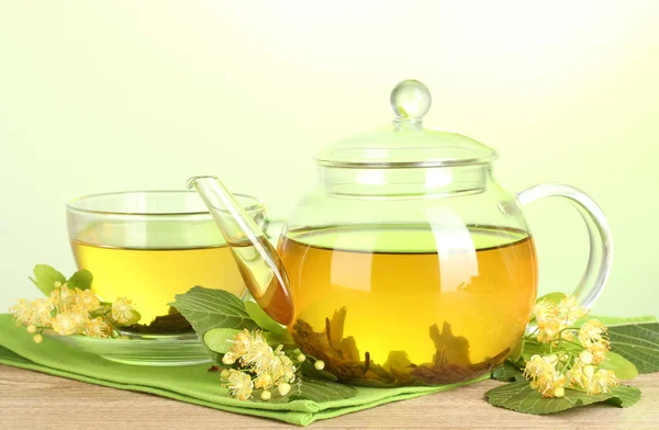 Teáskanna és a csésze linden tea és a virágok, a zöld háttér fából készült asztal — Stock Fotó