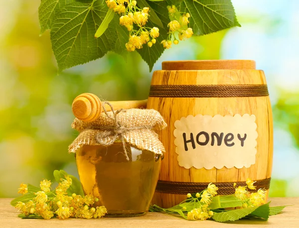 Jar och fat med linden honung och blommor på träbord på grön bakgrund — Stockfoto